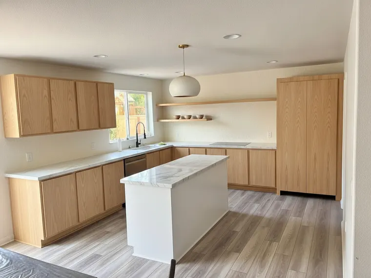 Japandi kitchen idea: flat white oak cabinets with no handles, warm white lime-wash walls, a pale limestone counter and one oak shelf with stoneware bowls