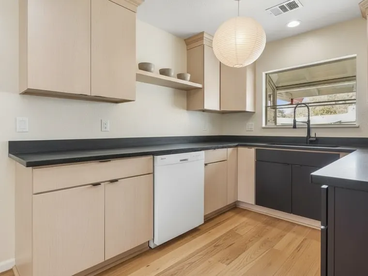 Japandi kitchen idea: flat pale ash cabinets with no handles, honed black soapstone counters, one oak shelf with stoneware bowls and a paper lantern pendant