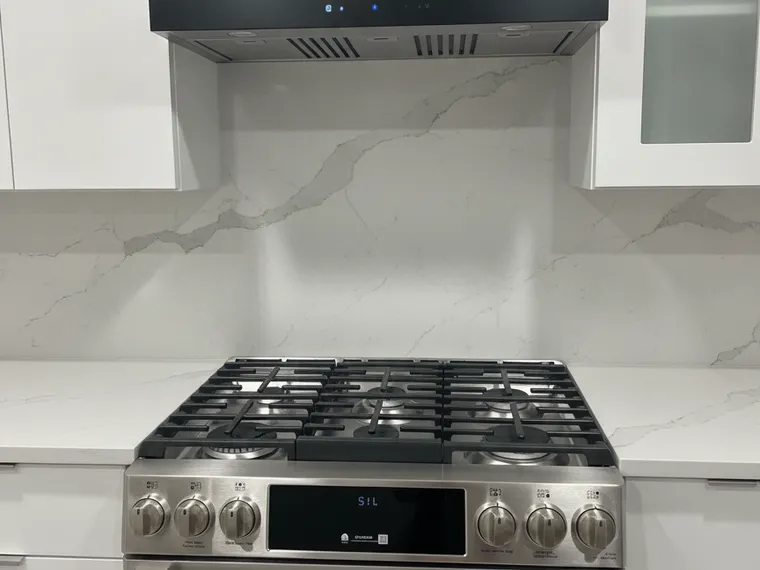 Modern kitchen idea: matte white flat-panel cabinets with a full-height marble-look slab backsplash and black range hood
