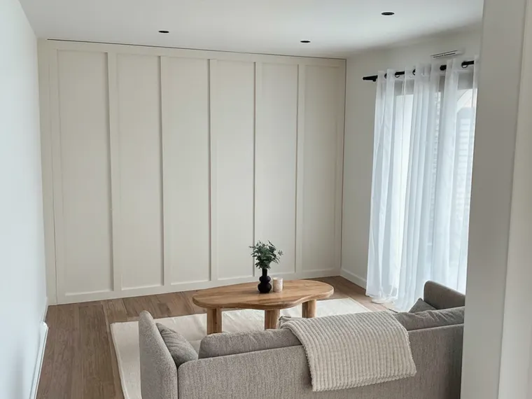 Wall paneling idea: full-height board and batten accent wall painted warm white behind a grey sofa