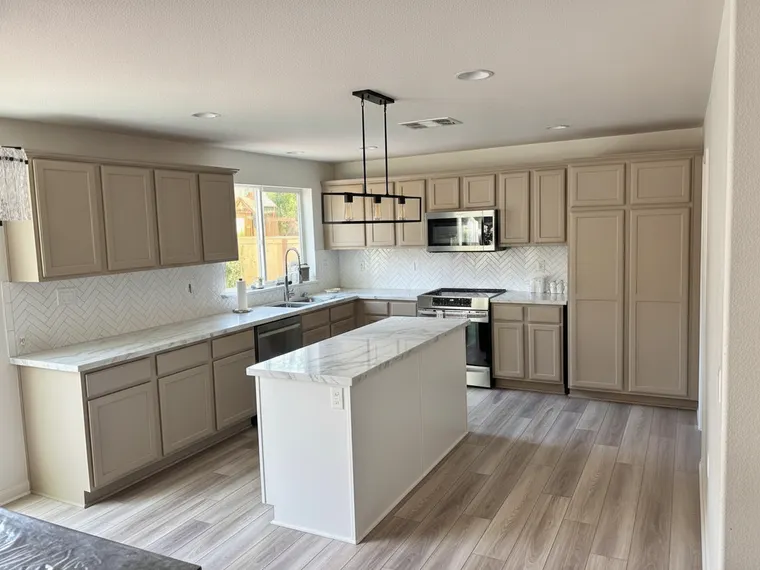 Modern kitchen idea: the same shaker cabinets in warm greige with a marble-look quartz island and a single linear black pendant