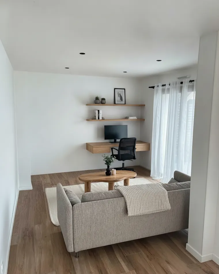 Small office idea: wall-mounted floating oak desk with a monitor, a chair and two floating shelves on the far wall of a living room, sofa kept