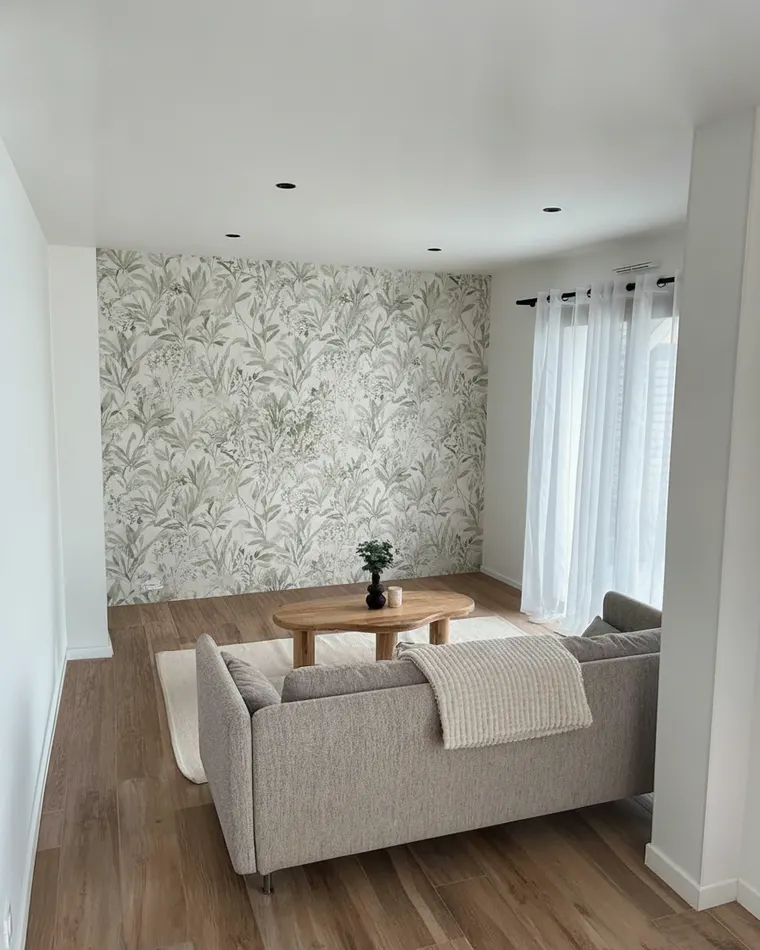 Wallpaper accent wall living room idea: large-scale muted botanical mural in greens and cream behind a grey sofa