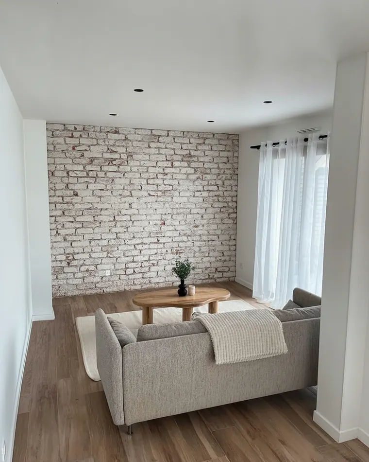 Brick accent wall living room idea: whitewashed exposed brick feature wall behind a grey sofa