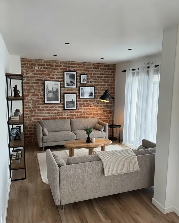 Industrial living room idea that keeps the layout: exposed red brick wall behind the sofa with black-framed prints, black metal floor lamp, black steel and wood shelving