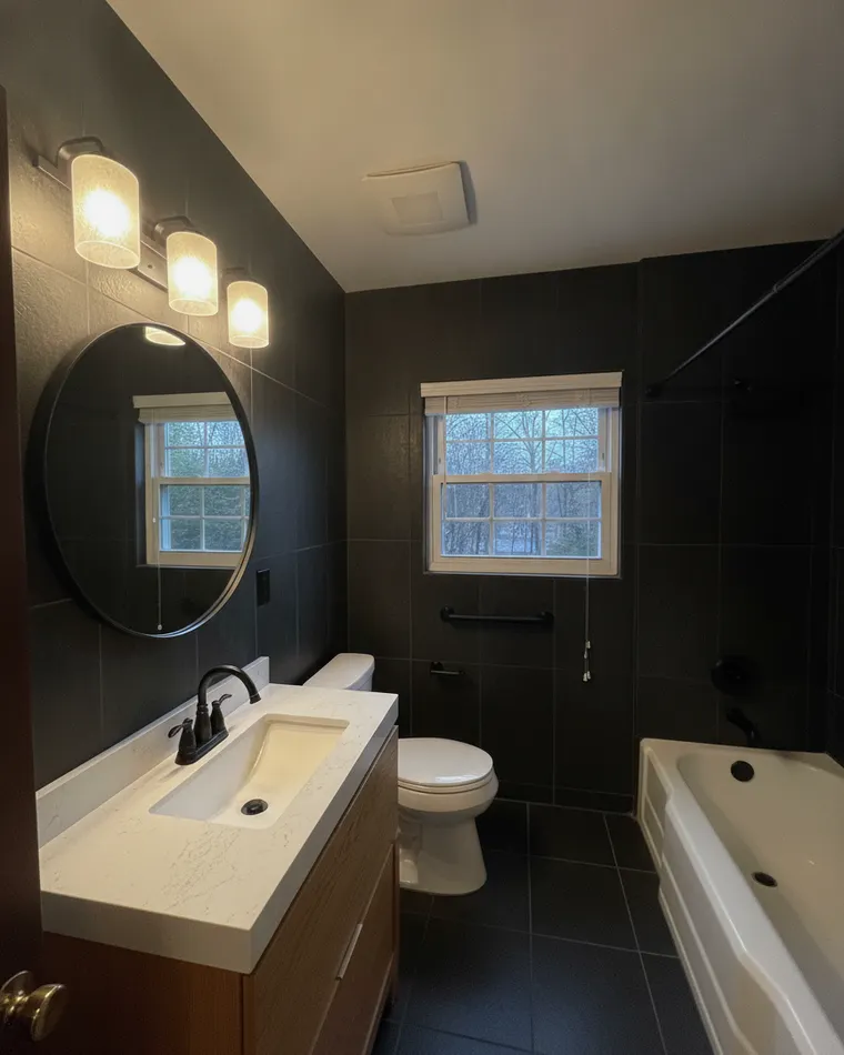 Warm black bathroom idea: matte black tile with a natural oak floating vanity and round mirror
