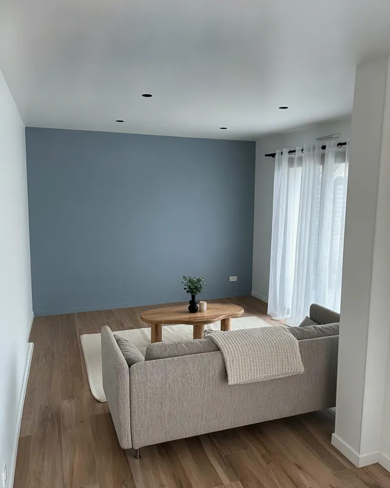 Living room paint color idea: dusty blue-grey walls with a grey sofa and white ceiling in a bright room
