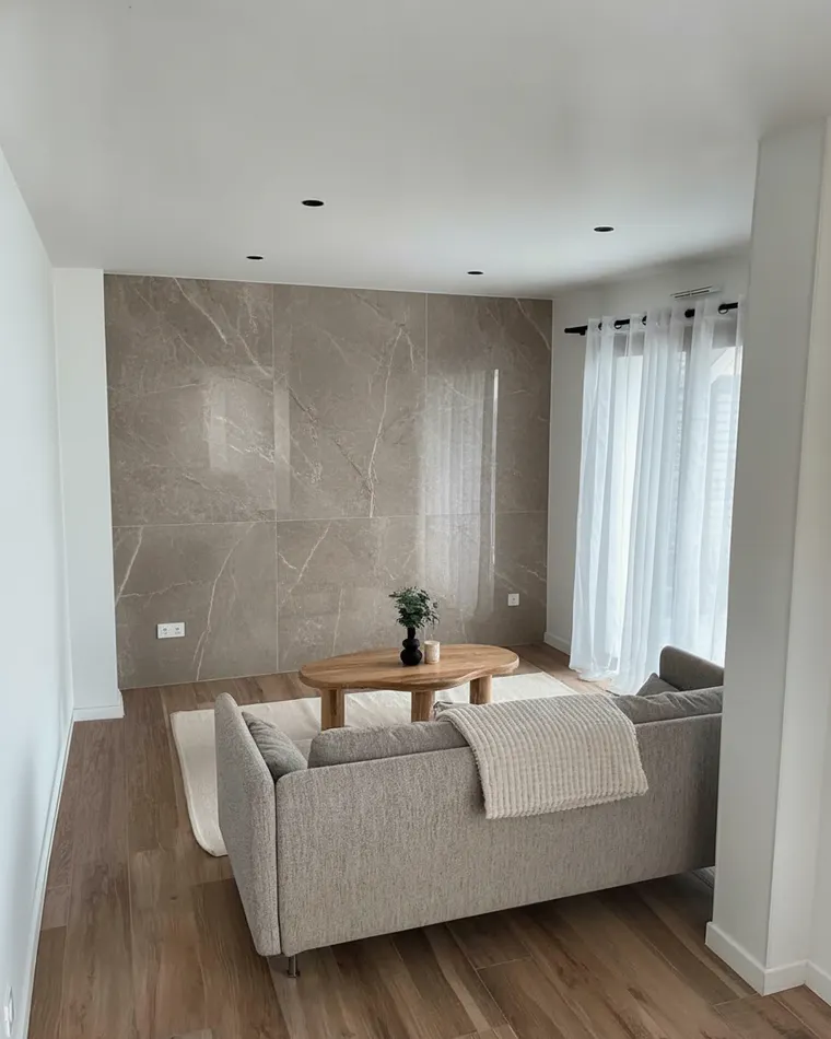 Stone accent wall living room idea: large-format warm grey marble-look slabs on the wall behind a sofa