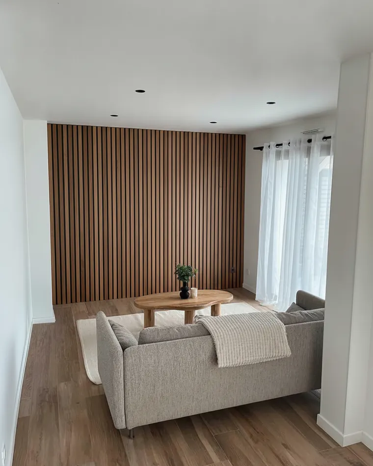 Wood accent wall living room idea: floor-to-ceiling vertical walnut slat wall with black backing behind a grey sofa