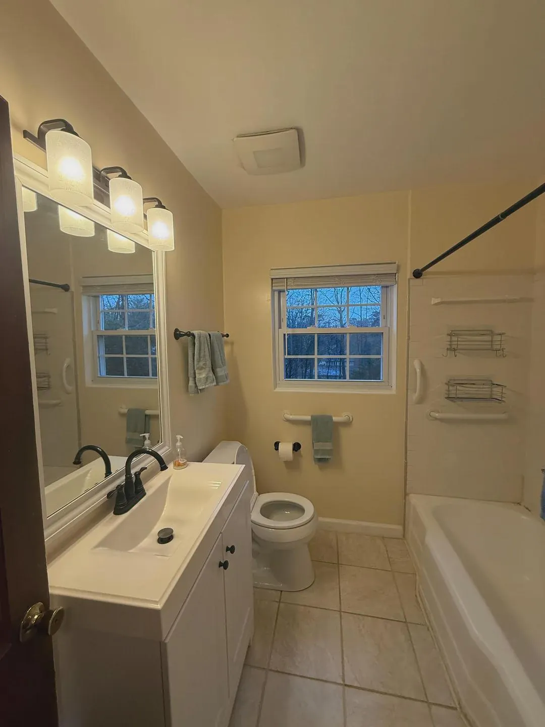 Dated bathroom with beige walls, white vanity, and tub-shower combo