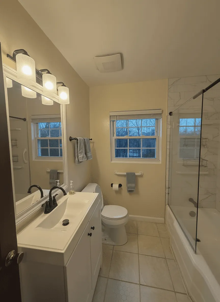 Same bathroom transformed with marble accent wall around tub and glass shower door
