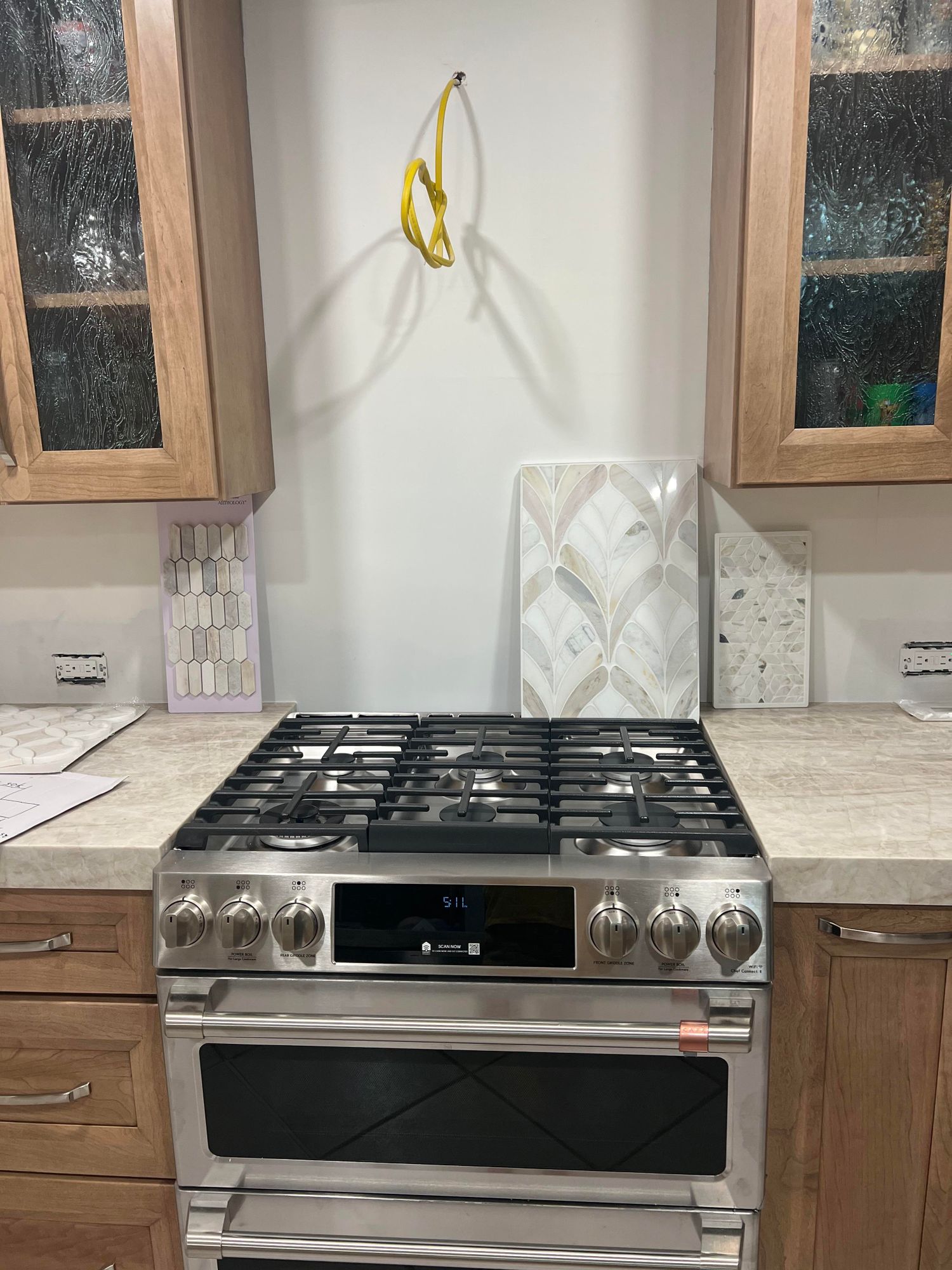 The original kitchen — warm honey cabinets, cream counters, bare backsplash wall with tile samples propped up
