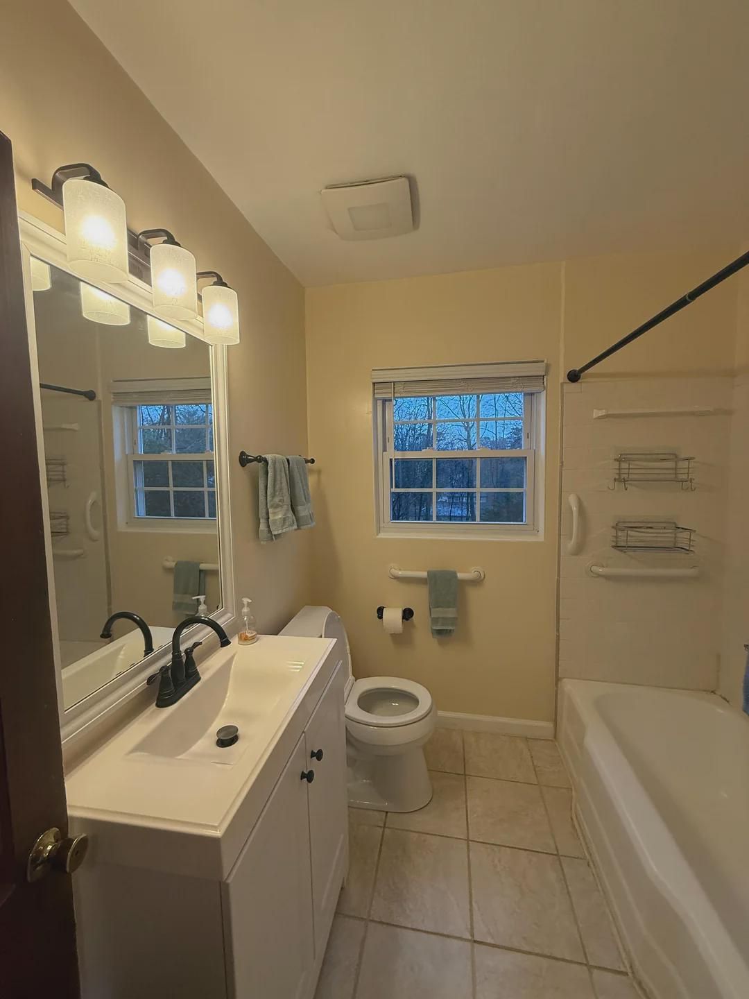 The original bathroom — yellow walls, beige tile floor, fiberglass tub surround with wire shelving