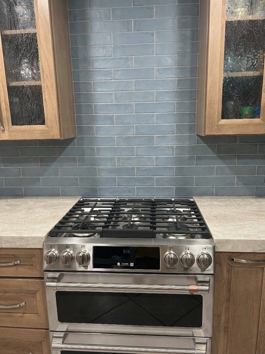Dusty blue subway tile backsplash against honey wood cabinets and cream countertops