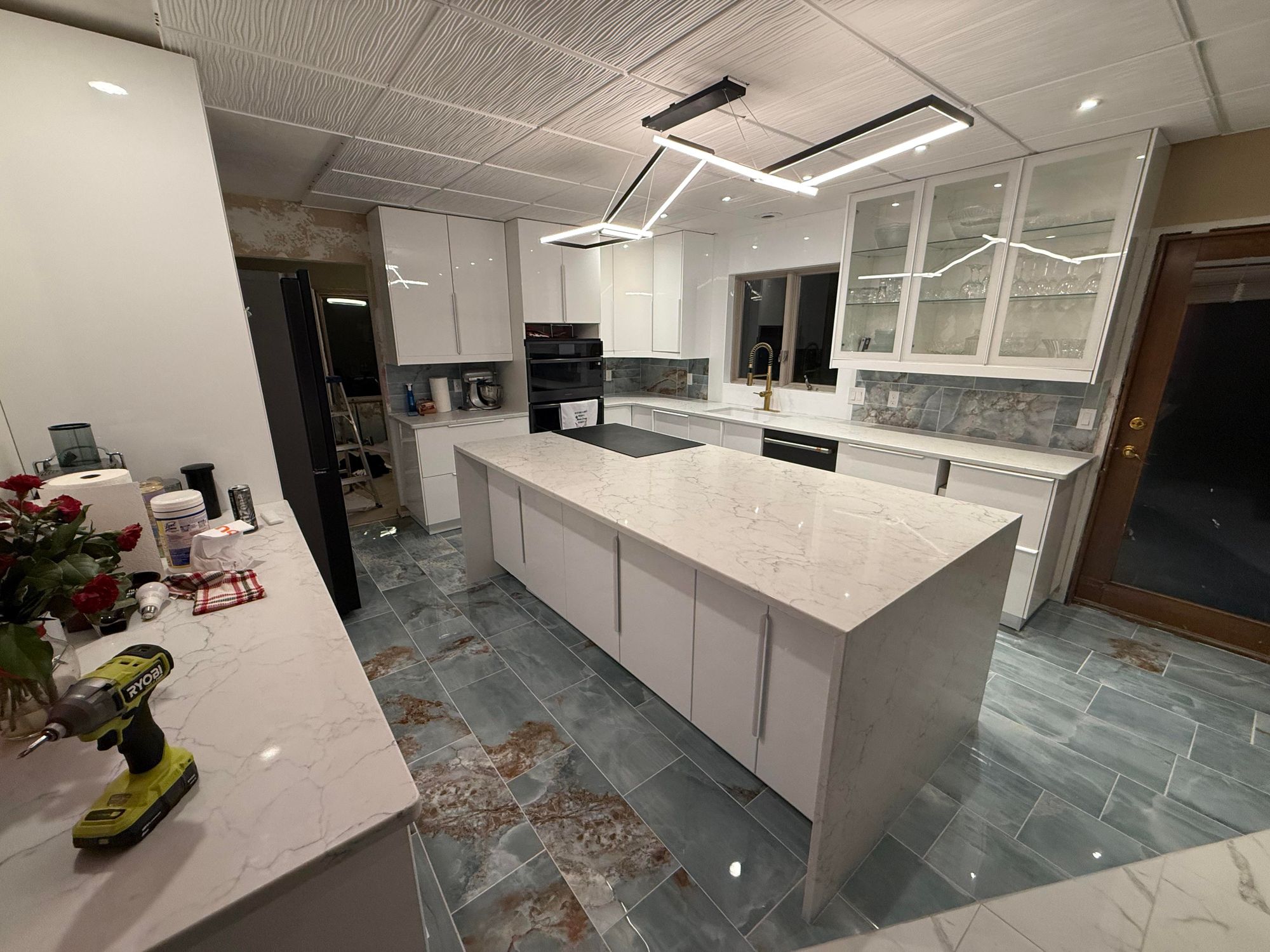 The original kitchen — white gloss cabinets, blue-gray floor, drop ceiling panels, harsh linear light